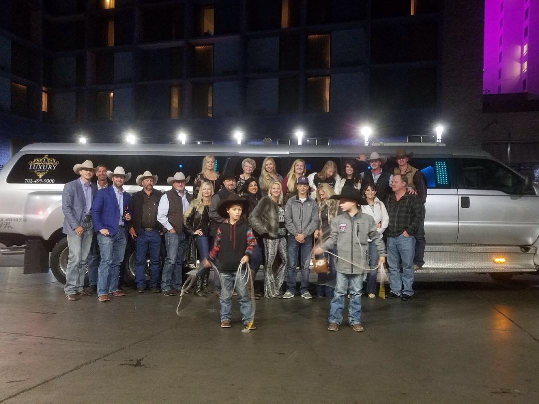 Large group of adults in western wear posing in front of a silver party bus at night Las Vegas