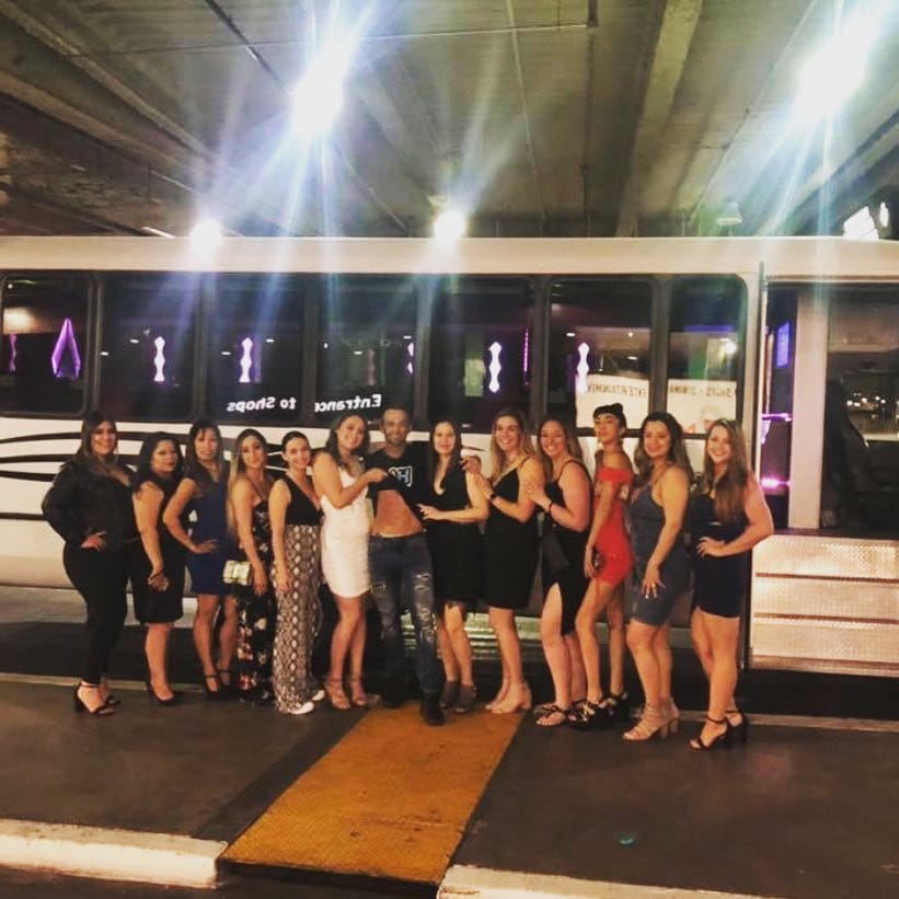Large group of women in party attire posing in front of a white party bus at night Las Vegas